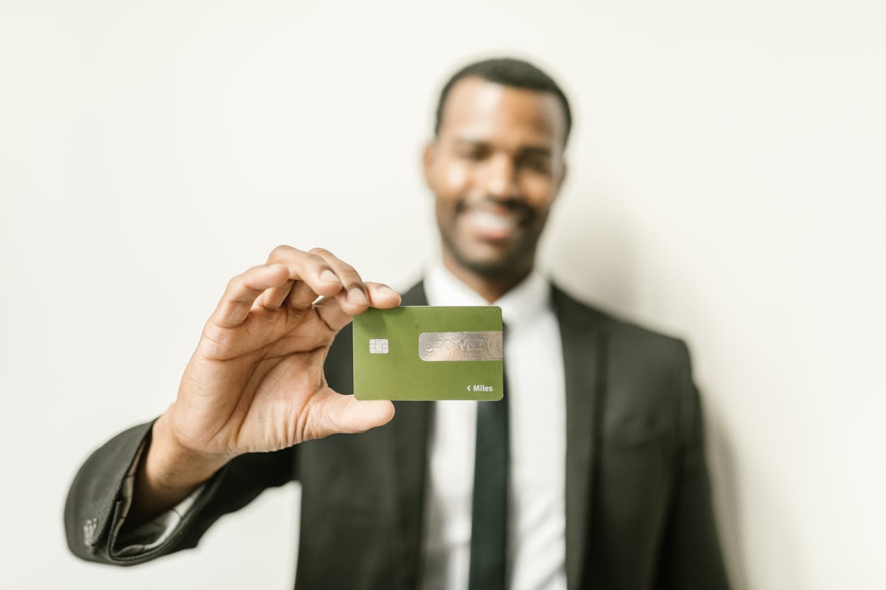 Smiling man in a suit holding a green credit card, showcasing finance and commerce.